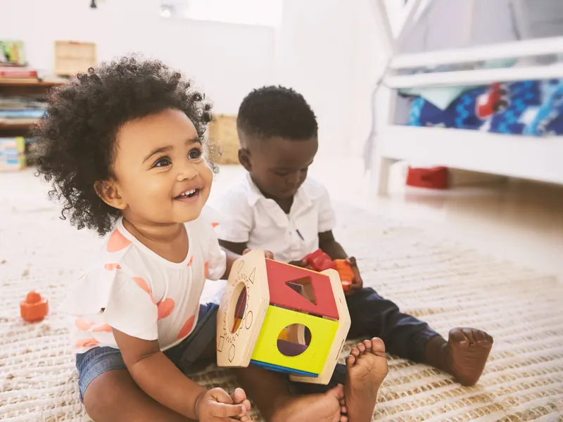 Two babies playing with a shape sorter